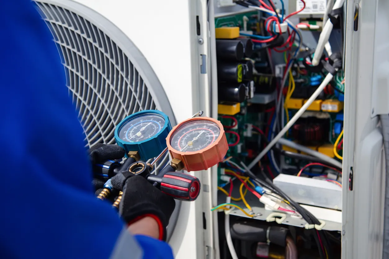 Technician reading refrigerant gauges on an air conditioning condenser